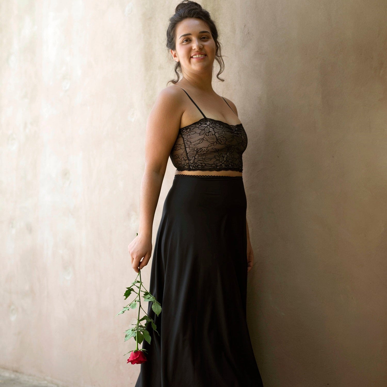 A woman standing against a wall wearing a black skirt with a lace top