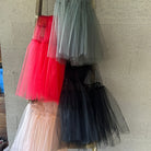 Tulle skirts in red, black, and white hanging on a rack against a stone wall.