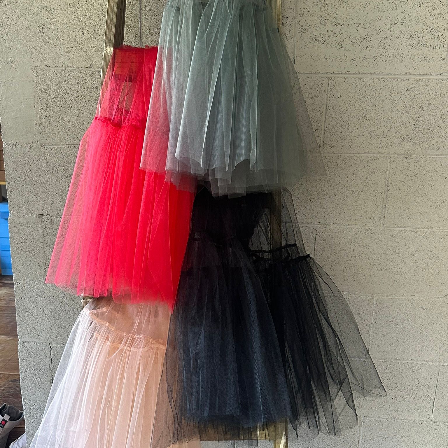 Tulle skirts in red, black, and white hanging on a rack against a stone wall.